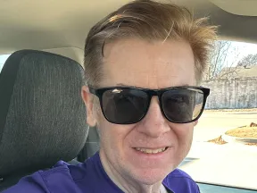 A man wearing sunglasses and a purple t-shirt.